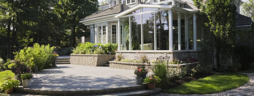 Brick and stone cottage style home with sunroom, patio and landscaped backyard